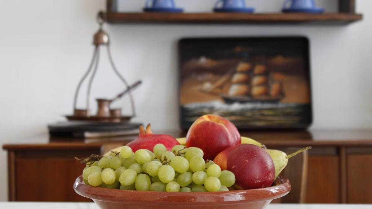 A vibrant bowl of assorted fruits on a table inside a Greek home, showcasing decorative elements.