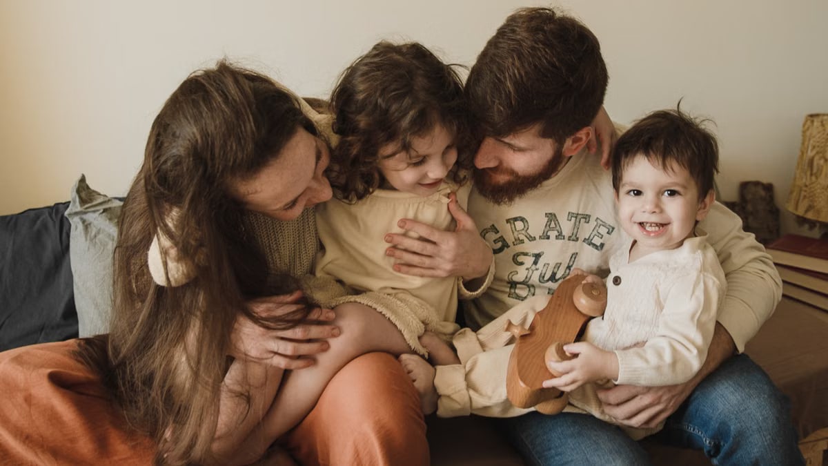 A joyful family moment with parents and children embracing and laughing together indoors.