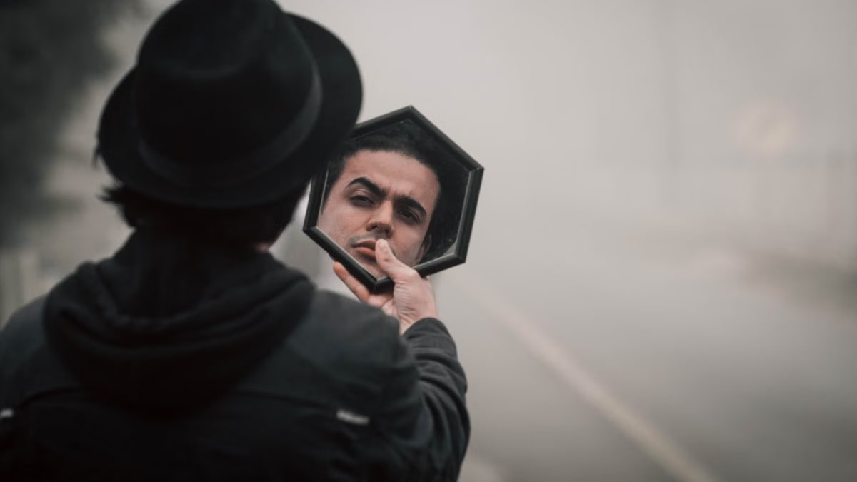 A mysterious man in a black hat reflects in a mirror on a foggy road.